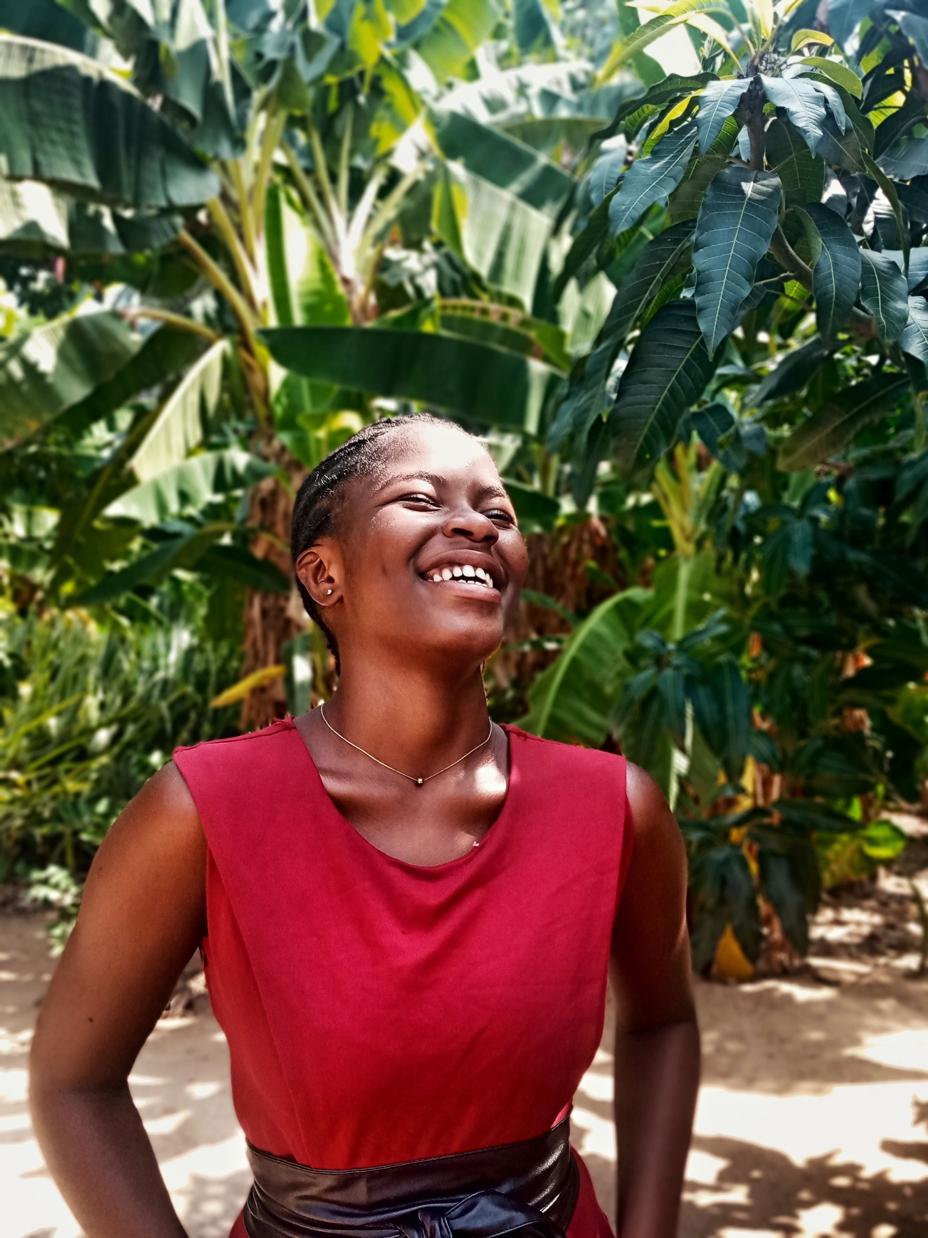 A woman laughing in daylight, against broad green leaves.