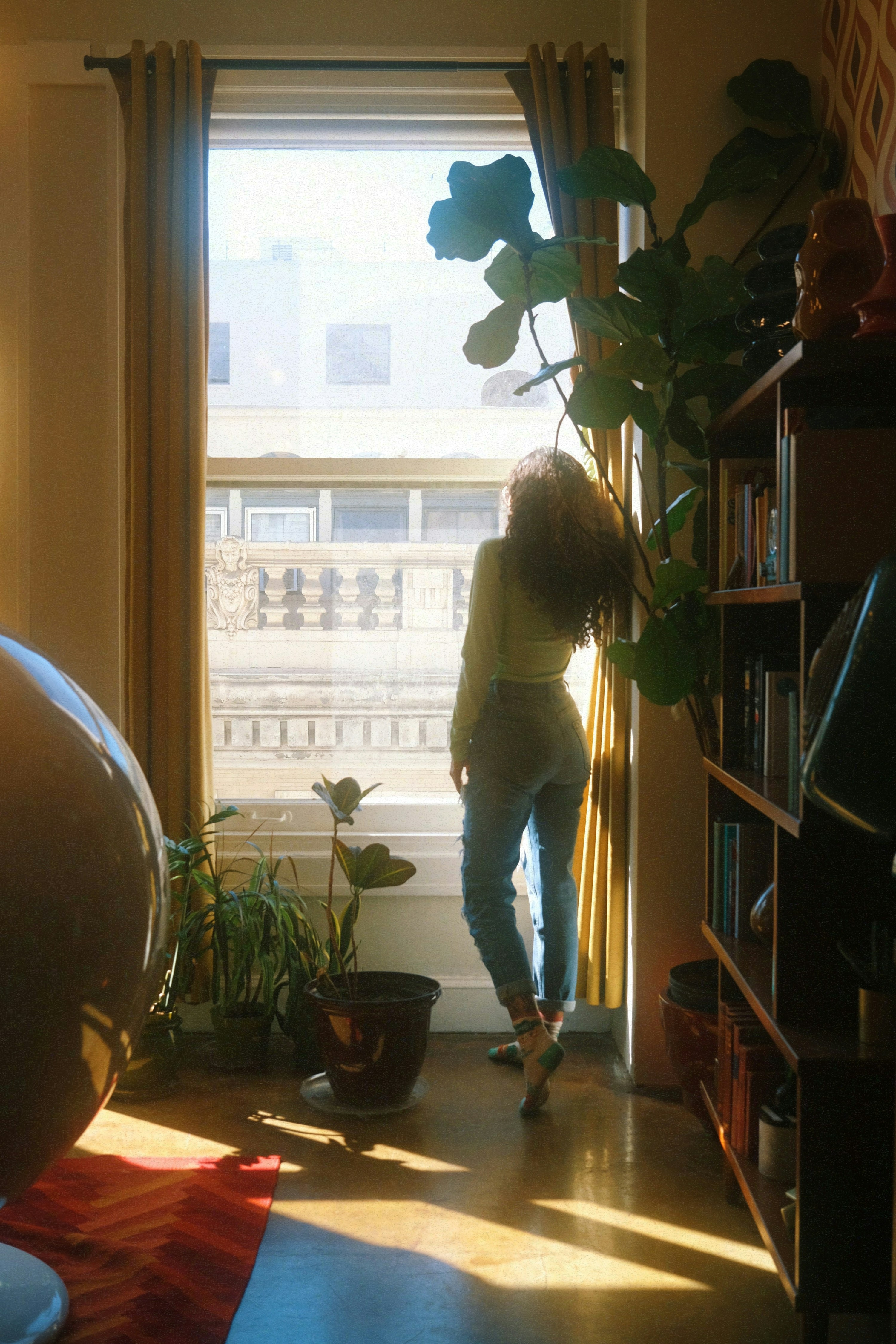 A woman at a sunlit window at home, surrounded by houseplants.